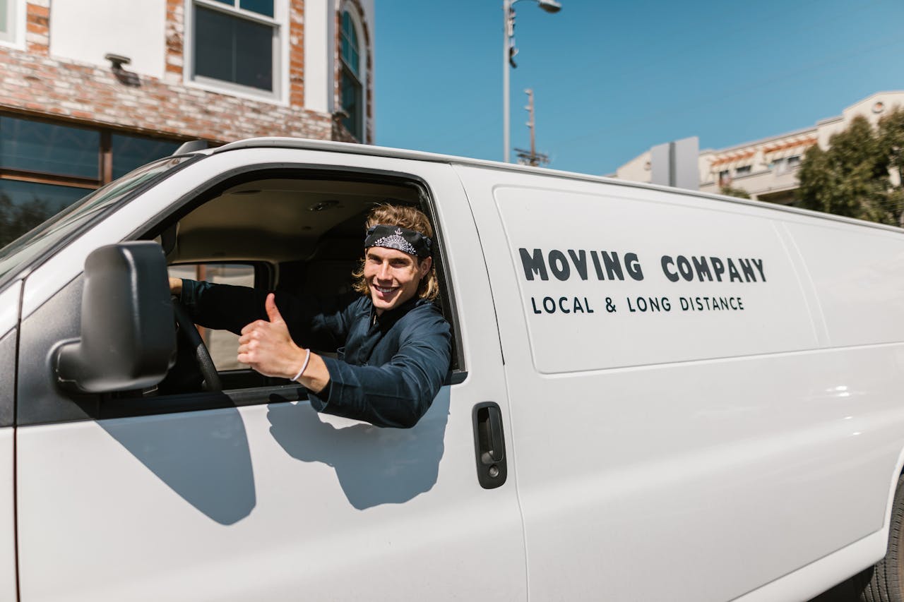 creative-03 Smiling mover giving thumbs up from a moving company van parked outside.
