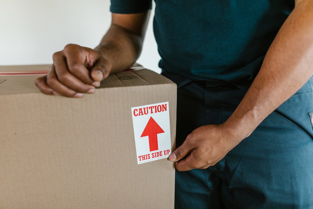mobile-01 A person handling a moving box with a 'caution this side up' label indoors.